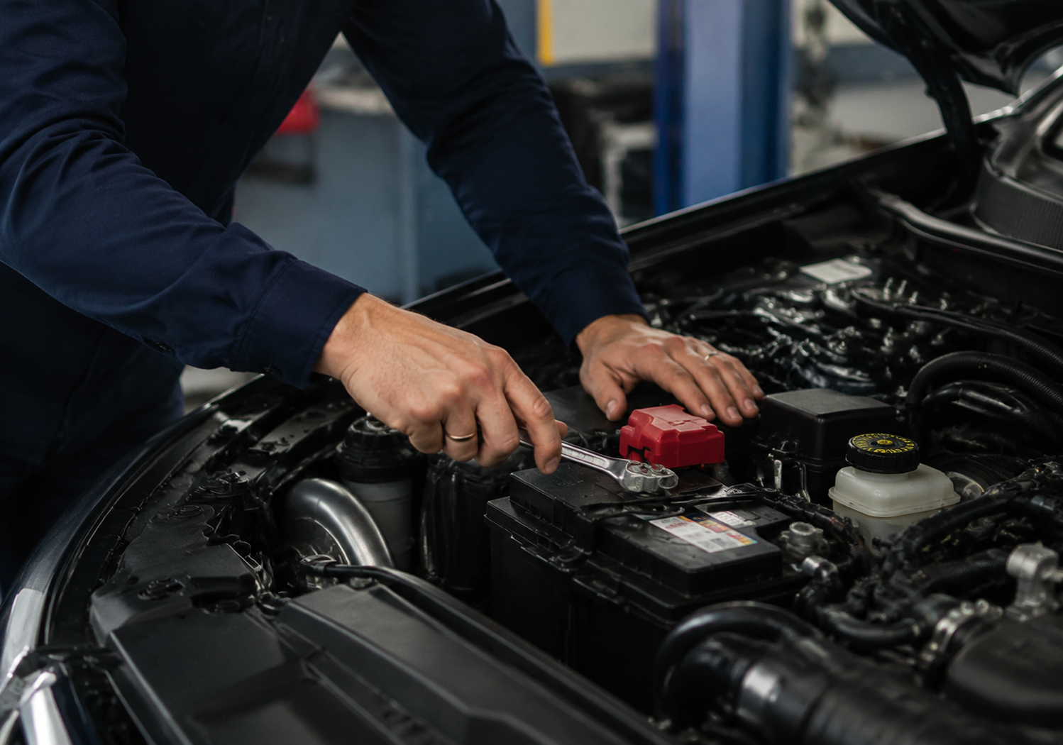 Professional automotive mechanic working inside an auto repair workshop, performing battery terminal inspection and engine maintenance on a car, representing Coventry Fixcore mobile mechanic and repair service with focus on diagnostics and vehicle care.